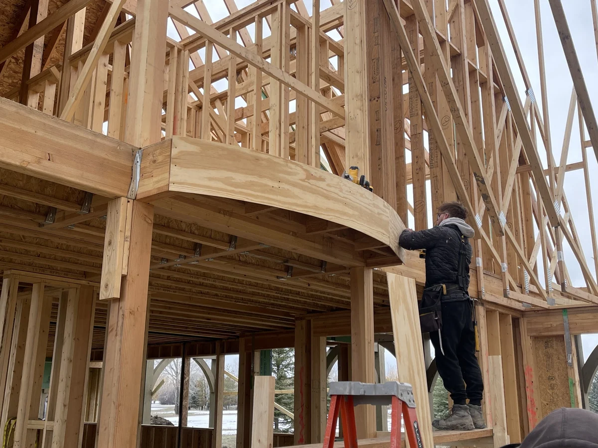 A carpenter working on a curved radius balcony framed into a tall open great room on a custom home