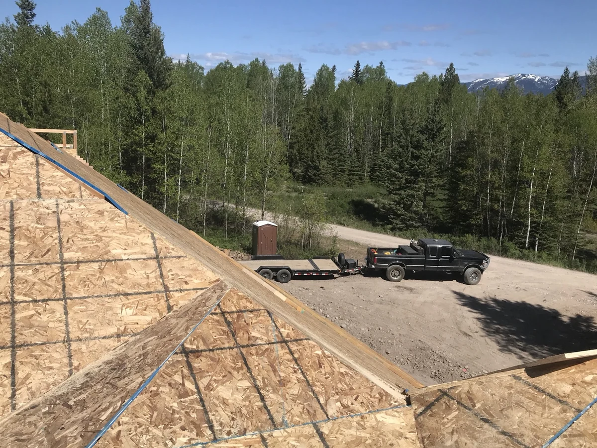 Roof sheathing going down across two valleys on a steep hip roof, with the Bitterroot mountains behind